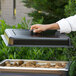 A person holding a black rectangular lid open over a tray of food.