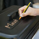 A hand writing "Chafing Dish" on a black lid for a chafing dish.