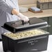A person wearing gloves holding a black chalkboard lid over a large casserole dish.