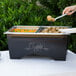 A person serving food from a Sterno ChalkBoard Chafer at a buffet table.