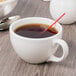 A Libbey ivory porcelain coffee cup filled with coffee and a spoon.