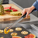 A hand using Vollrath Jacob's Pride tongs to grill pineapple slices.