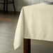 A square wooden table with a white tablecloth on it.