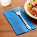 A fork on a Hoffmaster Marina Blue paper napkin next to a plate of pasta.