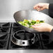 A person cooking broccoli in a Town hand hammered Cantonese wok over a stove.