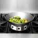 A Town hand hammered Cantonese wok with broccoli and carrots cooking in it on a gas stove.