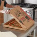 A person in an apron holding a Kraft corrugated pizza box.