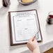 A hand holding a Thunder Group clear menu on a table in an Italian restaurant.