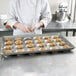 A woman in a white coat and gloves putting dough into a Chicago Metallic Hamburger Bun / Muffin Top / Cookie Pan.