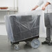 A man holding a plastic wrap over a black Cambro dish caddy.