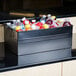 An American Metalcraft black rectangular hammered metal beverage tub filled with bottles of water on a counter.