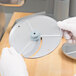 A person in white gloves holding a circular metal Robot Coupe 1/32" slicing disc.