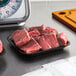 A black CKF foam meat tray with raw meat on a counter.