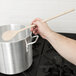 A hand holding a Tablecraft beechwood wooden spoon over a pot.