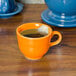 A Fiesta Tangerine china cup filled with tea and a tea bag on a table.