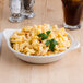 A Tuxton eggshell white bowl filled with macaroni and cheese on a table in a family-style restaurant.