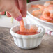 A hand dipping a shrimp into a white Carlisle ramekin of sauce.