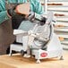 A man using an Avantco manual meat slicer to slice meat.