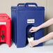 A person pouring a drink from a Cambro navy blue insulated beverage dispenser into a cup.