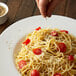 A person sprinkles Regal Fine Grind Ground Black Pepper on a plate of spaghetti.