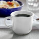 A white Tuxton round china cup filled with coffee on a saucer.