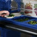 A person preparing food in a blue Cambro salad bar container.