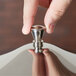 A hand holding a Vollrath chrome knob.