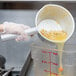 A person using a Vollrath aluminum dipper to pour liquid into a container.