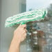 A hand cleaning a window with a Unger green and white StripWasher.