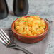 A Libbey terracotta bowl filled with macaroni and cheese with a fork next to it.