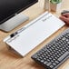 A person using a Quartet white frameless glass dry erase desktop pad on a wooden desk next to a computer.