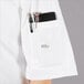 A person wearing a white Mercer Culinary chef jacket with a pocket holding a pen and phone.