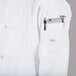 A person wearing a Mercer Culinary Millennia white chef jacket with a pocket full of tools and a cell phone.