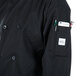 A person wearing a black Mercer Culinary Millennia long sleeve cook jacket with a phone and pen in a pocket.