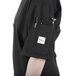 A person wearing a Mercer Culinary black chef jacket with pockets full of pens and a phone.