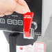 A hand pressing a red switch on a Bloomfield automatic coffee brewer.