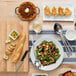 A table with Libbey Coos Bay pumpkin stoneware bowls of food and utensils.