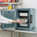 A woman using a Cambro front loading insulated food pan carrier in a professional kitchen.