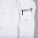 A person wearing a Mercer Culinary Millennia white cook jacket with a pocket full of tools and a cell phone.
