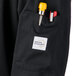 A black Mercer Culinary Millennia Air cook jacket with a pocket containing a pen and a yellow object.