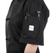 A person wearing a Mercer Culinary black chef jacket with a pen and phone in the pocket.