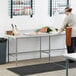 A woman standing at a Regency stainless steel work table in a kitchen preparing carrots.