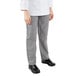 The legs of a person wearing Mercer Culinary Millennia Women's Houndstooth Chef Pants with a white coat and black shoes.