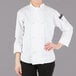 A woman wearing a white Mercer Culinary long sleeve chef jacket with cloth knot buttons.