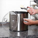 A person using a scoop to put ice cream in a Carlisle Black Coldmaster crock on a counter.