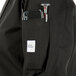 A person wearing a Mercer Culinary Millennia women's black chef coat with a phone and pen in the pocket.
