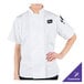 A woman wearing a white Mercer Culinary short sleeve chef jacket.
