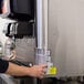 A woman using a Vollrath stainless steel cup dispenser on a countertop to fill a plastic cup.