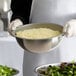 A person holding a Vollrath stainless steel mixing bowl of cheese.