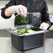 A person wearing gloves holding a clear Carlisle food container with a clear lid filled with food.